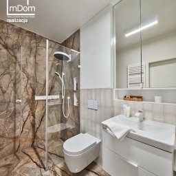 mDom Pracownia Projektowa - Nowoczesna łazienka z kabiną prysznicową typu walk-in wykończona marmurem w odcieniach brązu, biała wisząca toaleta i umywalka z szafką, widoczne logo firmy projektowej w lewym górnym rogu.