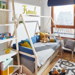 Pokój dziecięcy z łóżkiem w kształcie domku, drewnianym regałem, dywanem z motywem ulic i zabawkami budowlanymi, z napisem 'Franek' na ścianie i dekoracją okienną w kształcie koparki