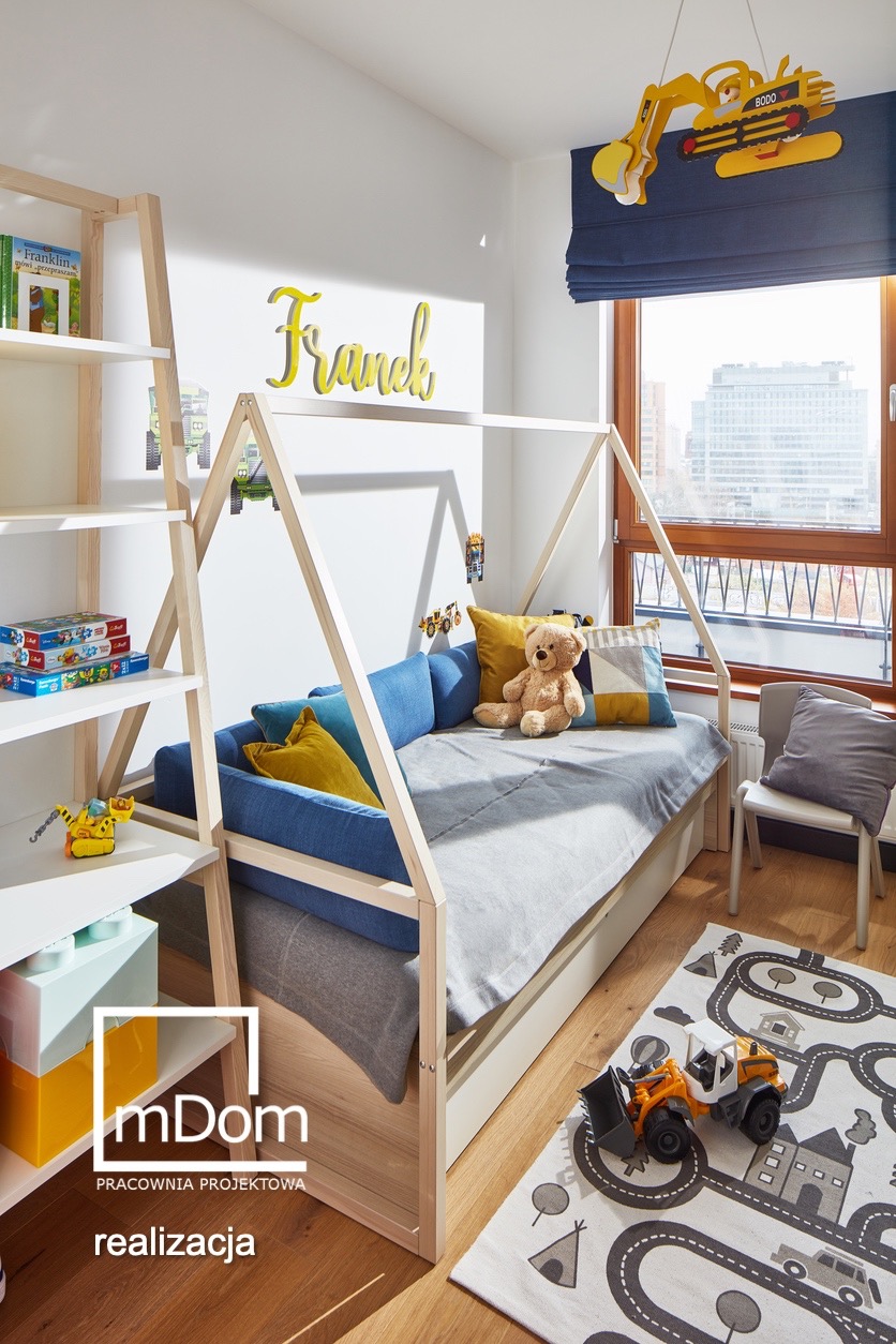 Pokój dziecięcy z łóżkiem w kształcie domku, drewnianym regałem, dywanem z motywem ulic i zabawkami budowlanymi, z napisem 'Franek' na ścianie i dekoracją okienną w kształcie koparki