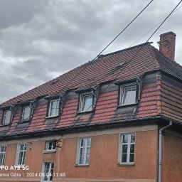 FAB DACH USŁUGI OGÓLNOBUDOWLANE - Ceglasty dach z lukarnami na kamienicy pod pochmurnym niebem. Widoczny komin i fragment elewacji. Dachówka karpiówka.