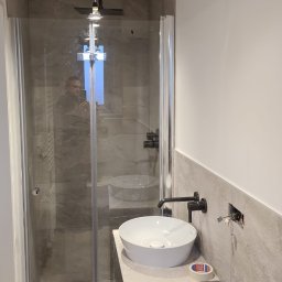 Marcin Rzeźnik - Nowoczesna łazienka z kabiną prysznicową typu walk-in, okrągłą umywalką nablatową i czarną armaturą, widoczne niedokończone prace elektryczne przy ścianie.