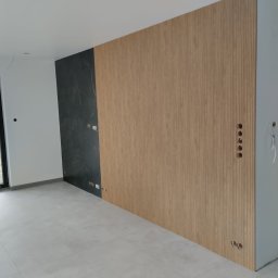 Marcin Rzeźnik - Nowoczesne wykończenie wnętrza: ściana z paneli drewnianych i płytek imitujących marmur, szara podłoga, widoczne gniazdka elektryczne. Minimalistyczny design.