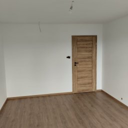 Marcin Rzeźnik - Wykończone wnętrze w Lipce: brązowe panele podłogowe, białe ściany i drewniane drzwi. Minimalistyczny design, surowa żarówka. Gotowe do umeblowania.