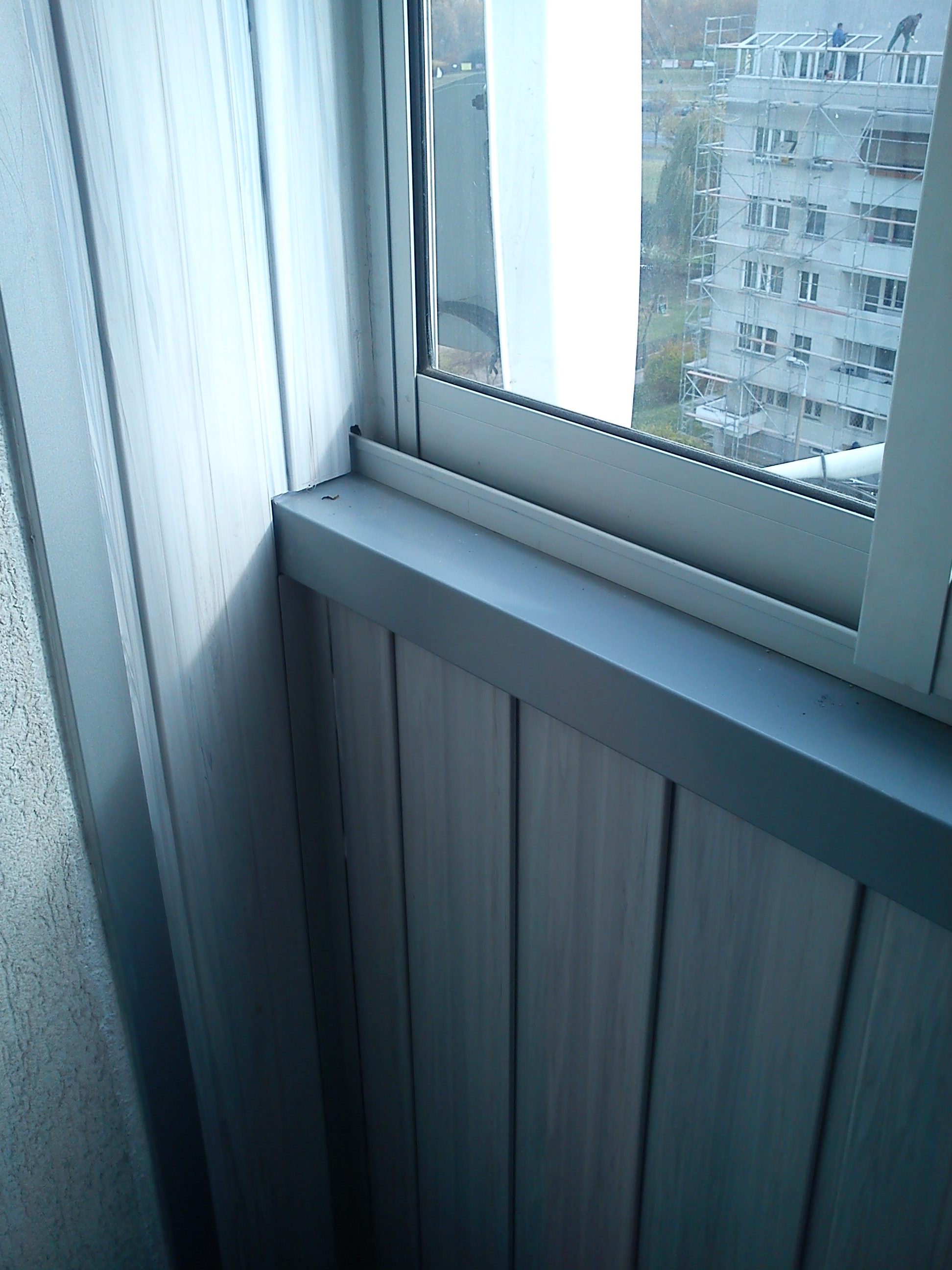 Oszklony balkon z widokiem na budynek w rusztowaniach i pracujących robotników.