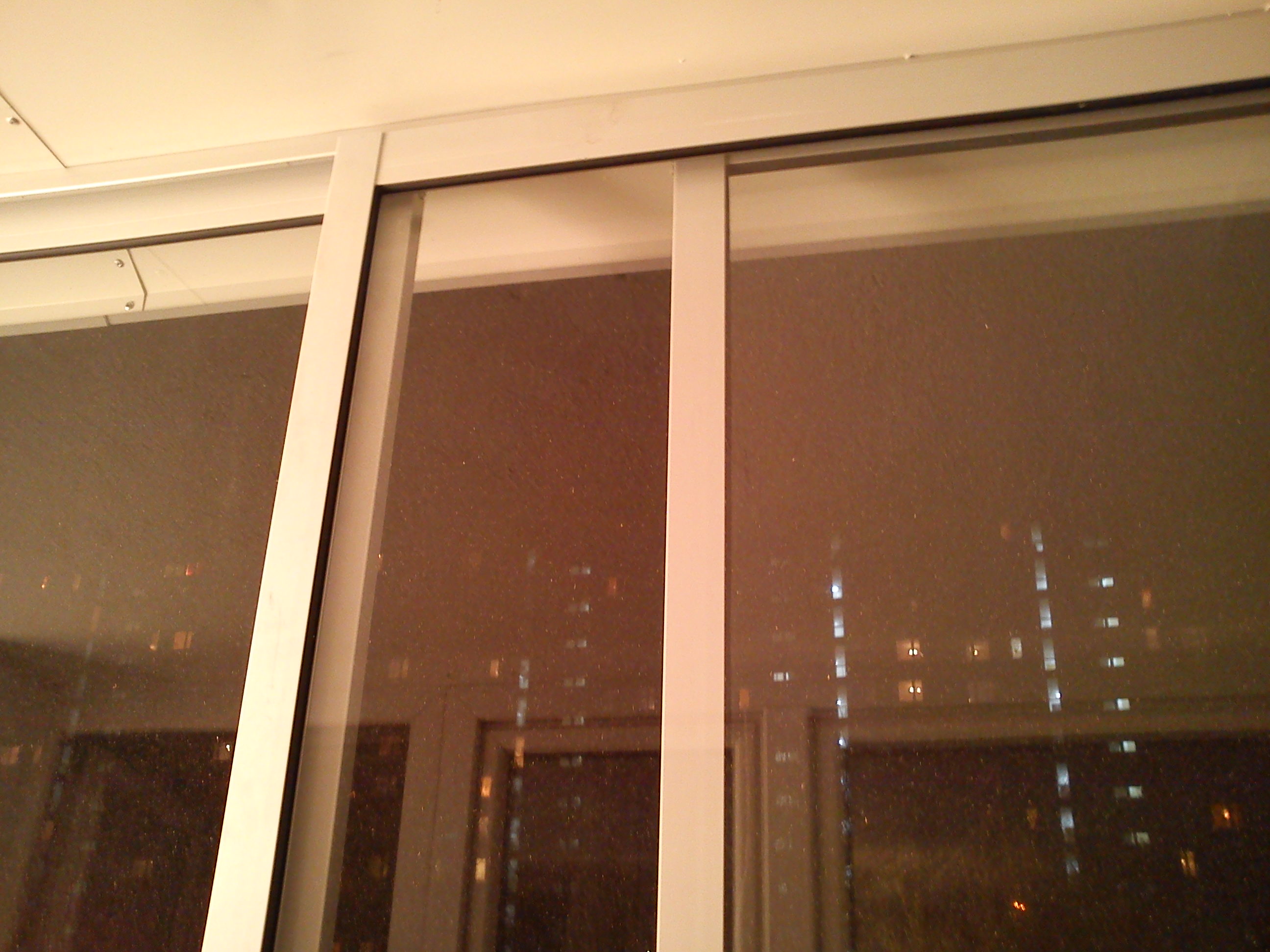 Zabudowa balkonu z przesuwnymi oknami; widok na nocne miasto z licznymi światłami.