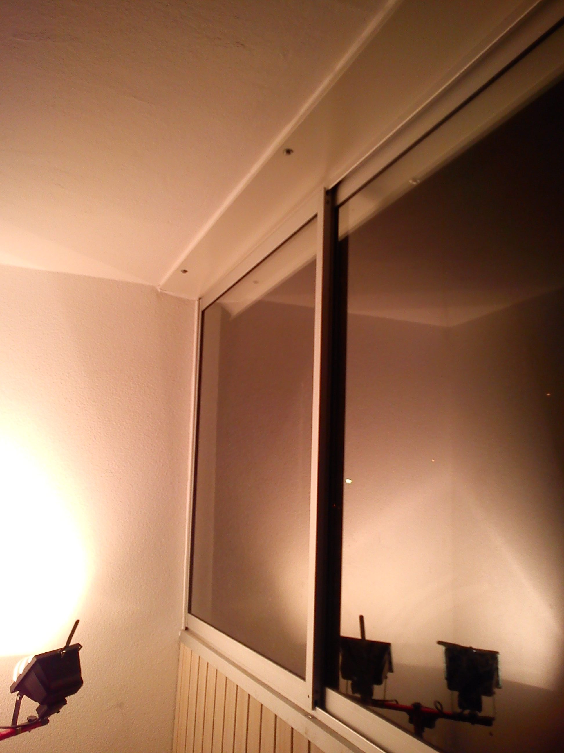 Zabudowa balkonowa z przesuwnymi oknami, widoczne elementy konstrukcyjne i odbicie lampy halogenowej.