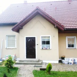 Dom jednorodzinny po nałożeniu tynku elewacyjnego, widoczne puszki z farbą, mały chłopiec i rusztowanie w tle.