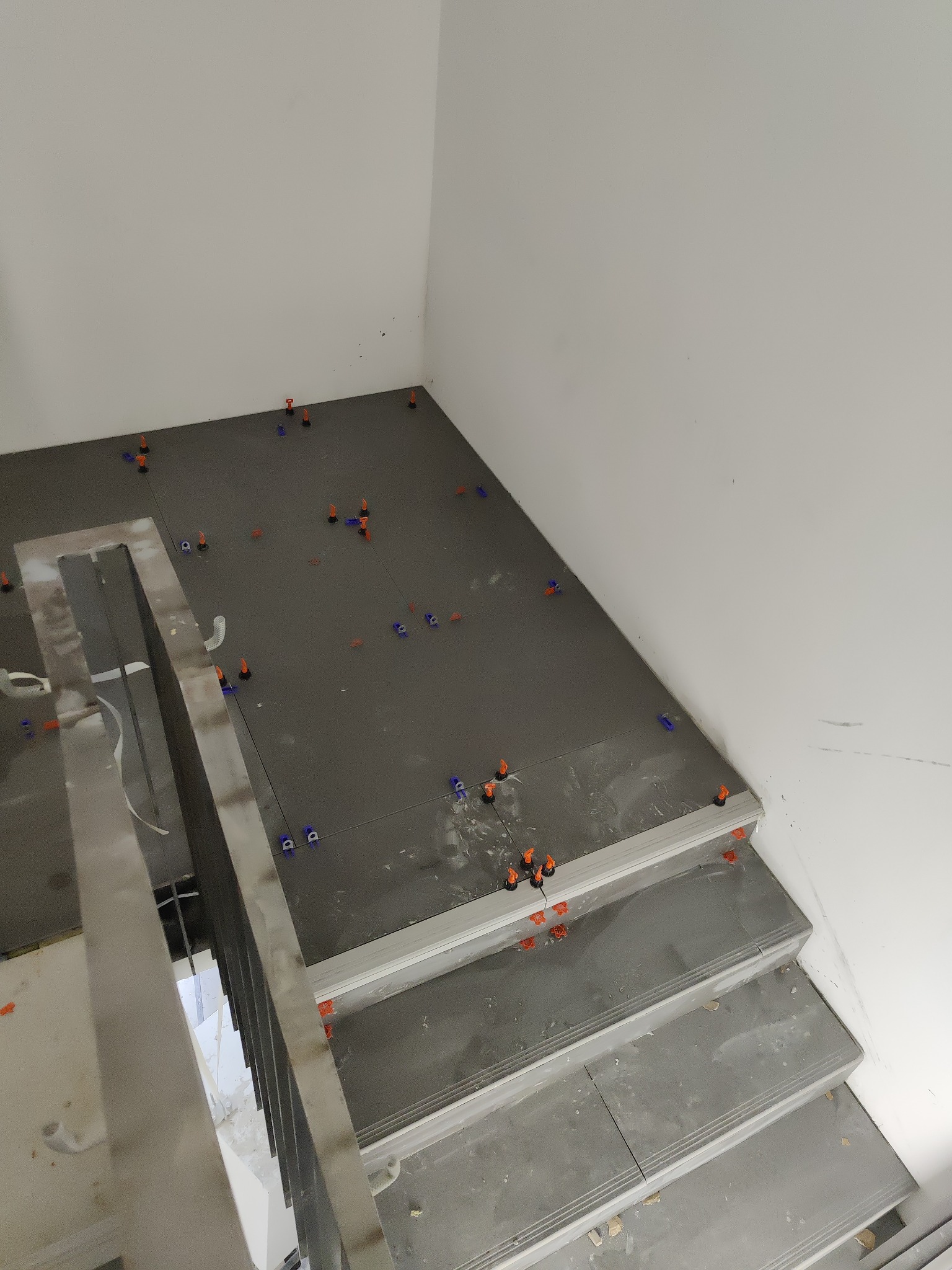 Układanie szarych płytek na schodach z użyciem systemu poziomowania płytek (klipsy i kliny).