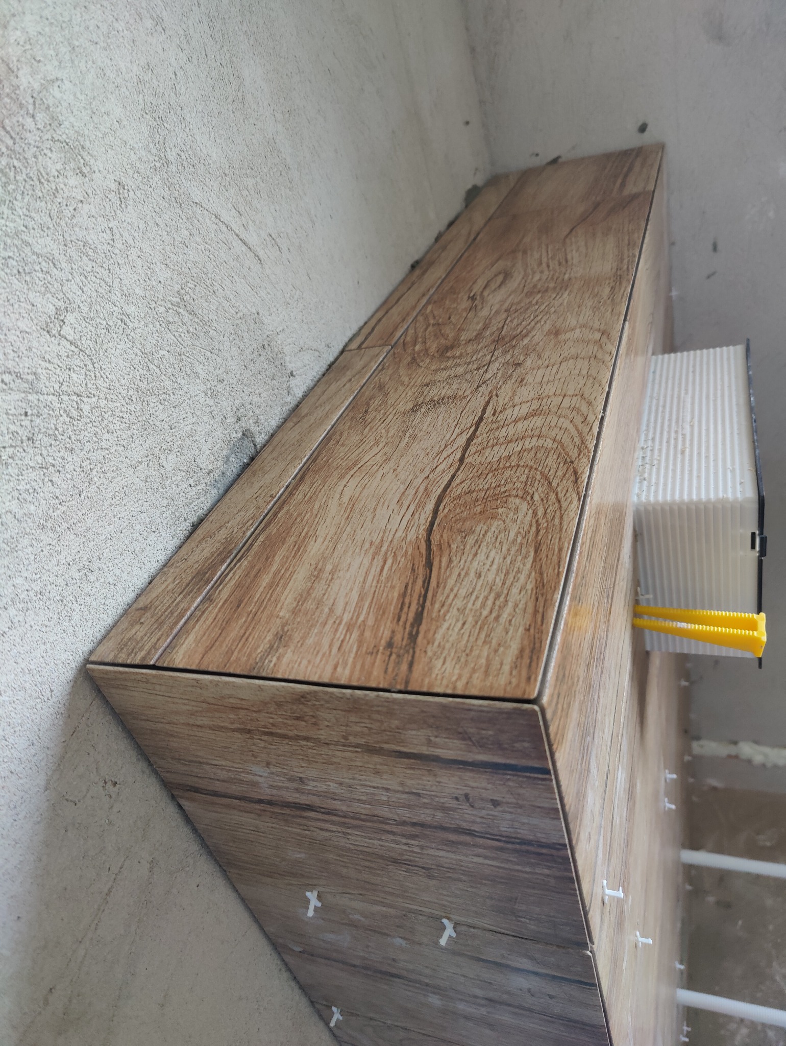 Układanie płytek imitujących drewno w narożniku; widoczne krzyżyki dystansowe i system poziomowania płytek.