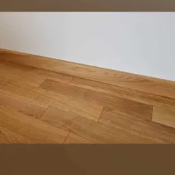 Ułożona podłoga z paneli drewnianych w odcieniach brązu, widok z niskiego kąta, przy białej ścianie.