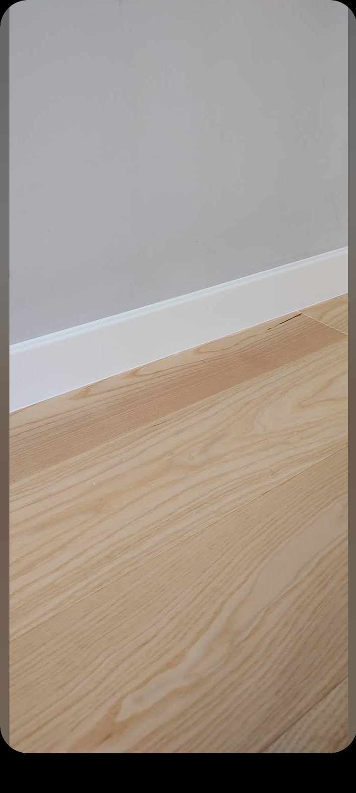 Jasny parkiet ułożony przy szarej ścianie z białą listwą przypodłogową, widoczne delikatne usłojenie drewna.