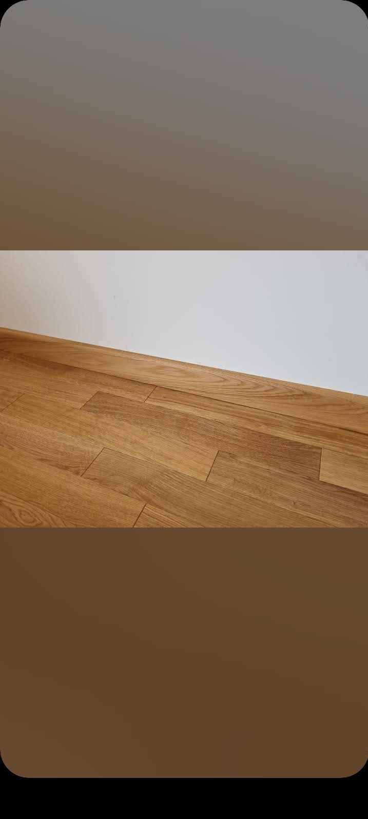 Ułożona podłoga z paneli drewnianych w odcieniach brązu, widok z niskiego kąta, przy białej ścianie.