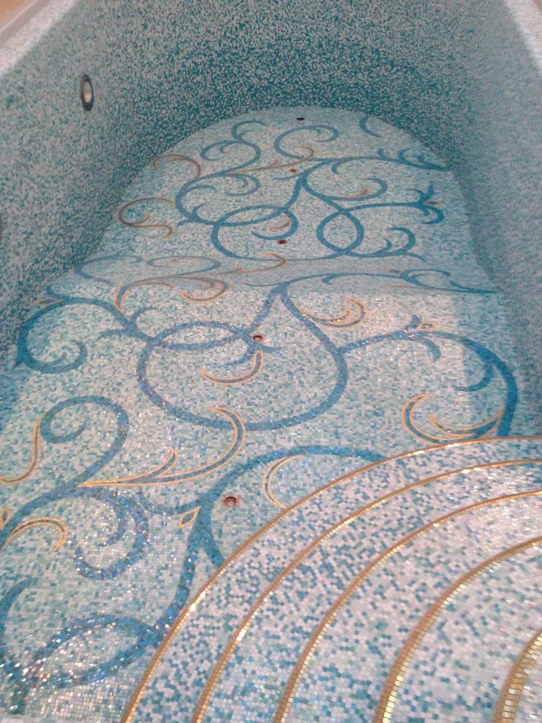 Mozaika w odcieniach błękitu i złota zdobi wnętrze kabiny prysznicowej, tworząc wzór roślinny na ścianach i podłodze.