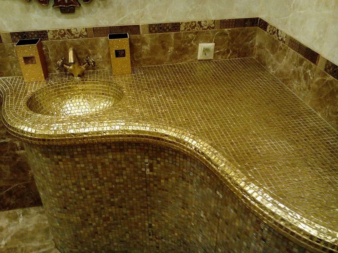 Złota umywalka mozaikowa z baterią i akcesoriami w luksusowej łazience wykończonej marmurem.