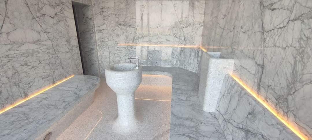 Nowoczesna łazienka wykończona marmurem z podświetleniem LED, obejmująca wolnostojącą umywalkę na postumencie oraz siedzisko wbudowane w ścianę.