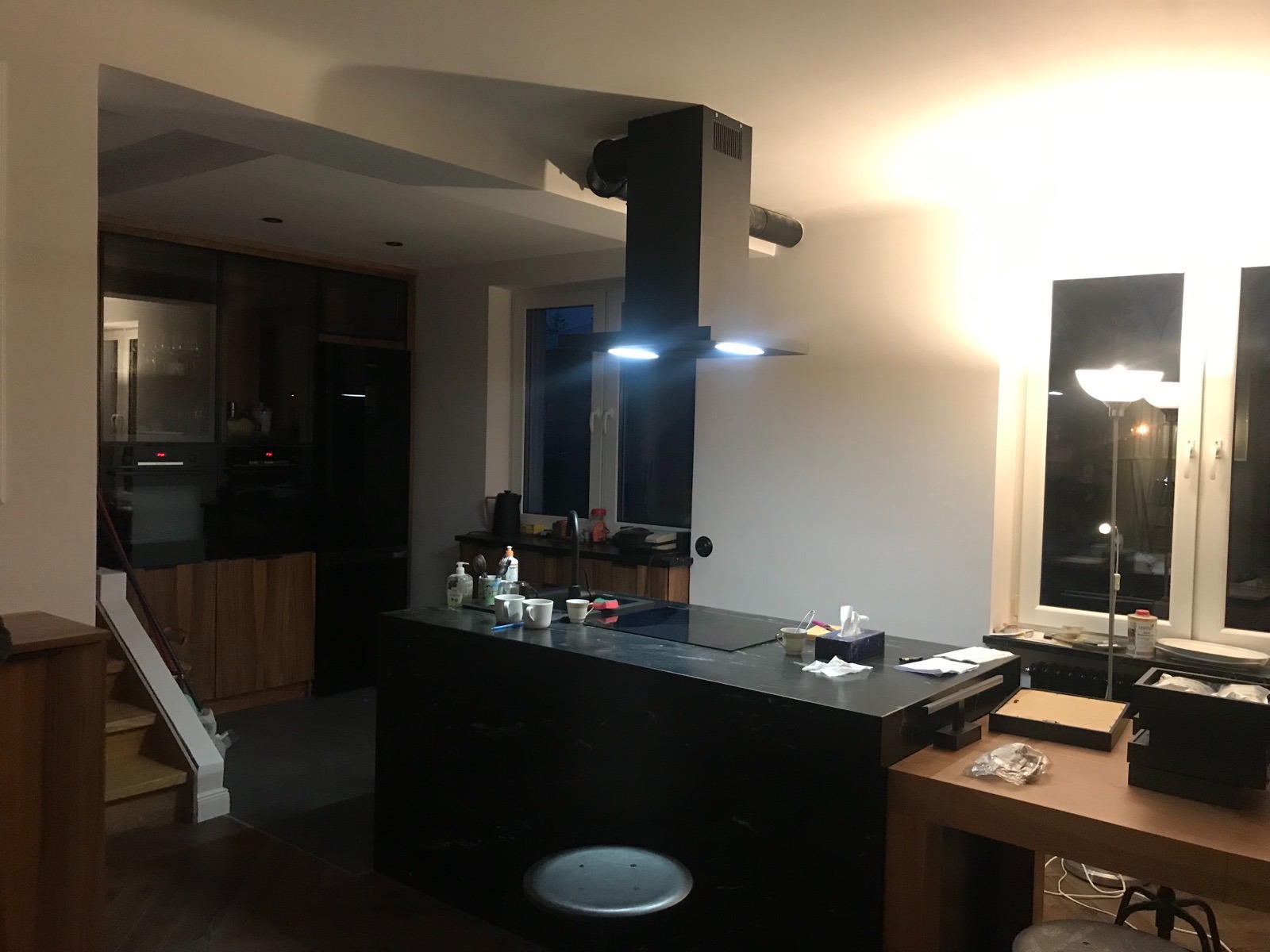 Nowoczesna kuchnia z czarną wyspą i okapem, widok na zabudowę kuchenną z drewnianymi frontami i schody w tle.