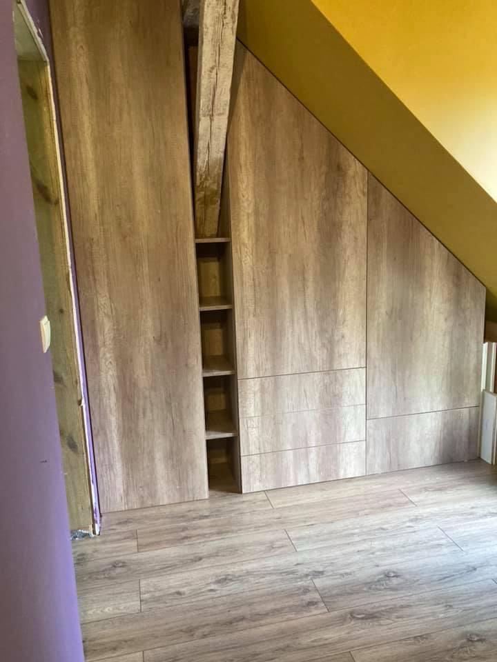 Szafa wnękowa z drewnopodobnymi frontami, dopasowana do skosu poddasza, z widoczną belką konstrukcyjną wkomponowaną w półki.