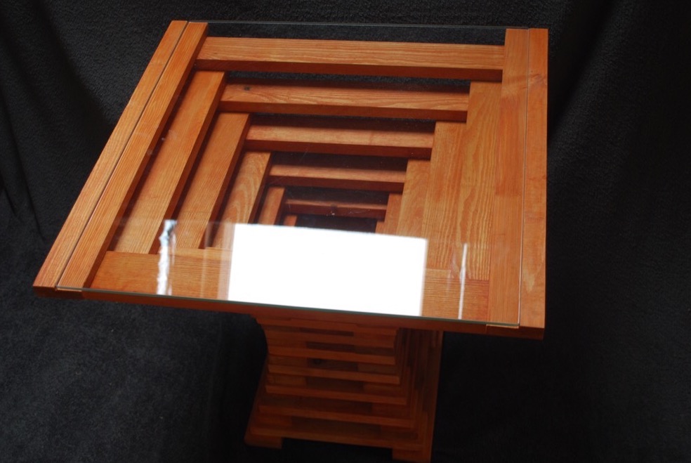 Nowoczesny stolik kawowy z drewna o geometrycznej podstawie i szklanym blacie, widok z góry pod kątem.