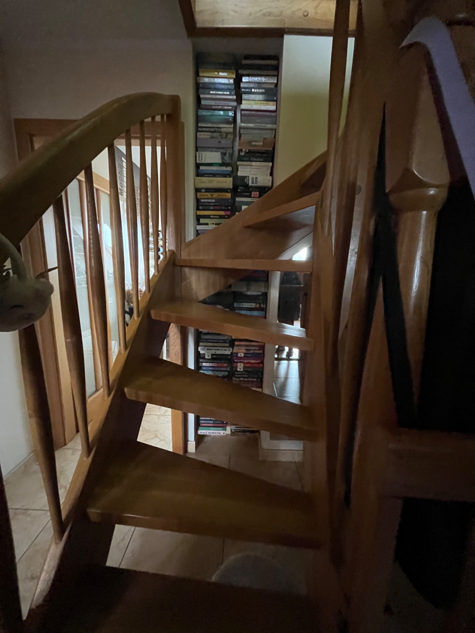 Drewniane schody z balustradą, widok z dołu, z półką na książki w tle.