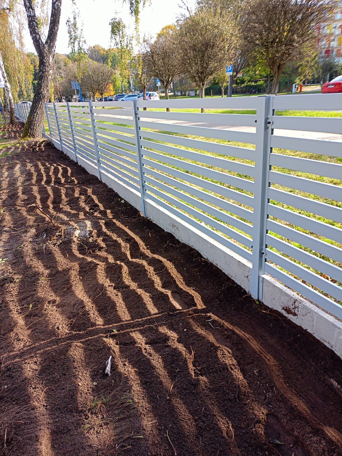 Nowoczesne ogrodzenie panelowe w Charzynie, z poziomymi przęsłami w kolorze szarym, zamontowane na betonowej podmurówce. Świeżo przekopana ziemia przed ogrodzeniem z wyraźnymi śladami po obróbce...