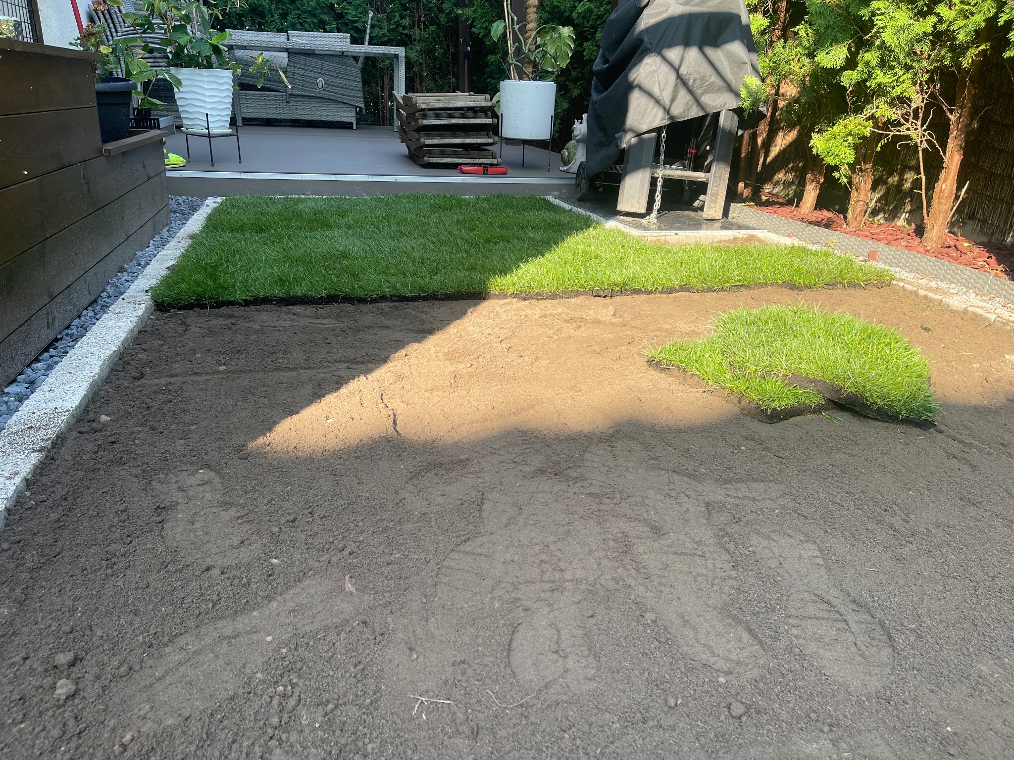 Układanie trawy z rolki w ogrodzie. Częściowo ułożona darń na przygotowanym podłożu, widoczne obrzeża i elementy dekoracyjne ogrodu.