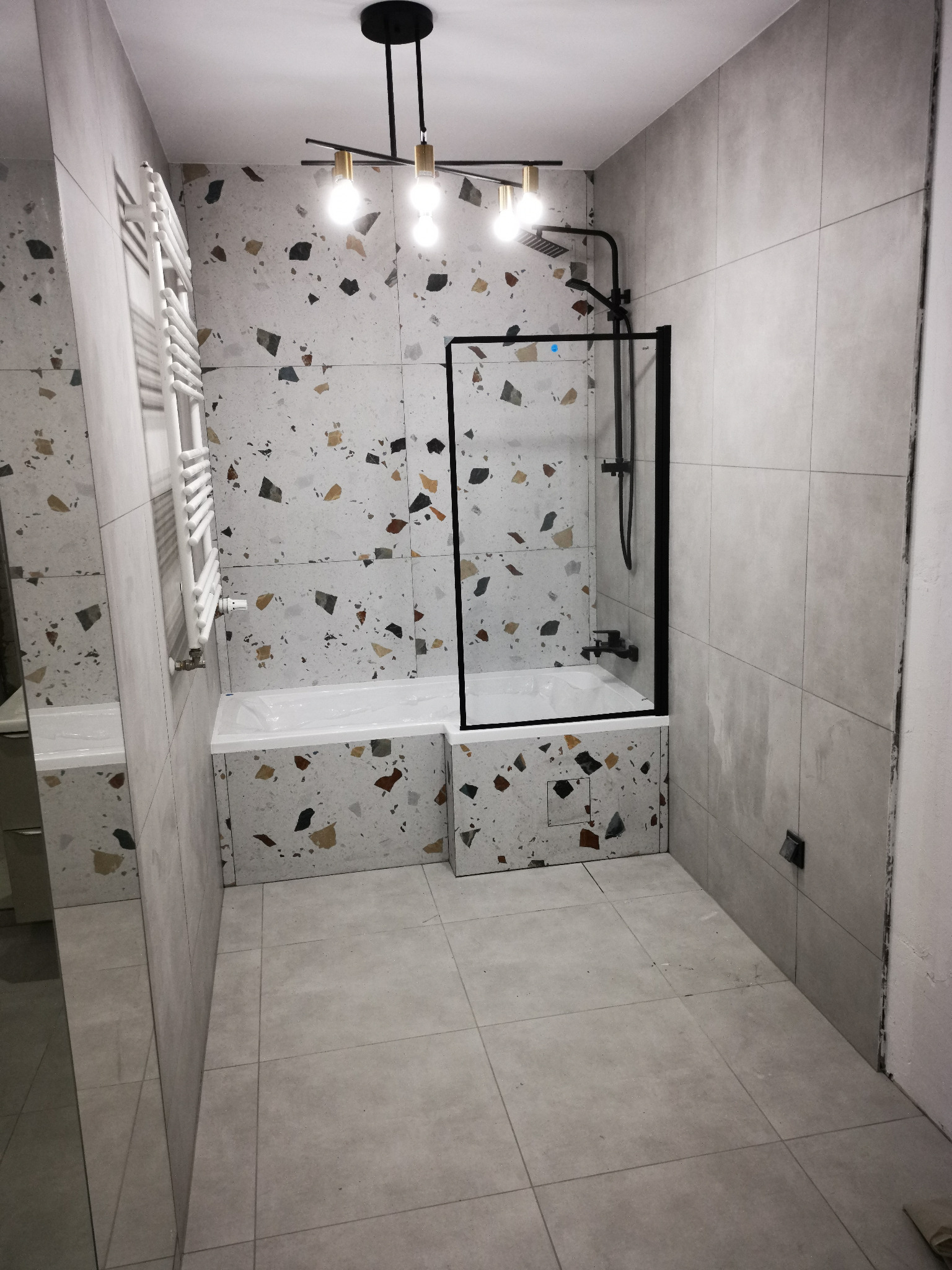 Nowoczesna łazienka z wanną obudowaną płytkami lastryko, czarną kabiną prysznicową i designerską lampą sufitową z żarówkami Edison