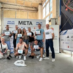 MKrawczyńska team - Grupa uśmiechniętych uczestników Półmaratonu Praskiego pozuje z numerami startowymi na tle mety i mapy trasy, w hali z surowymi betonowymi kolumnami.