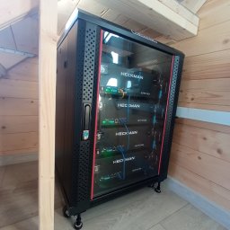 Samowystarczalni.eu Sp. z o.o. - Czarna szafa rack Heckman z zainstalowanymi urządzeniami, umieszczona w drewnianym pomieszczeniu z jasną podłogą, widok z boku.