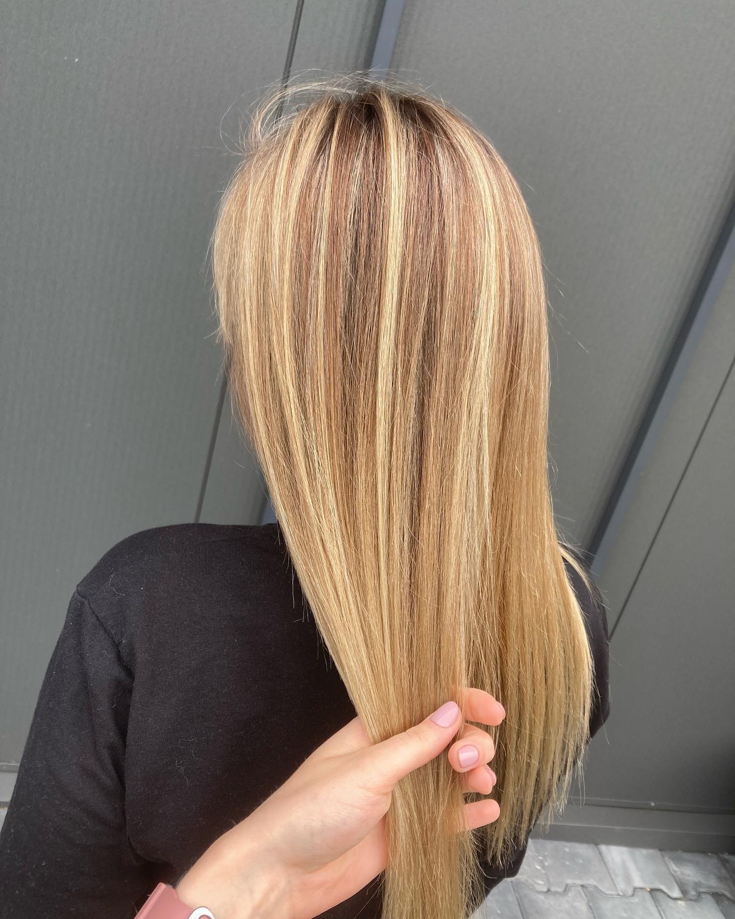 Blond włosy z pasemkami, widok z tyłu, dłoń dotyka włosów, paznokcie pomalowane na jasny róż.