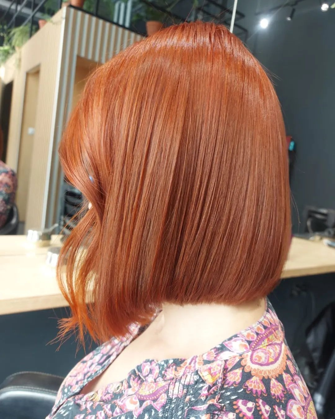 Świeżo ostrzyżone, lśniące, miedziano-rude włosy w stylu bob, z delikatną falą po jednej stronie, prezentowane na tle salonu fryzjerskiego.