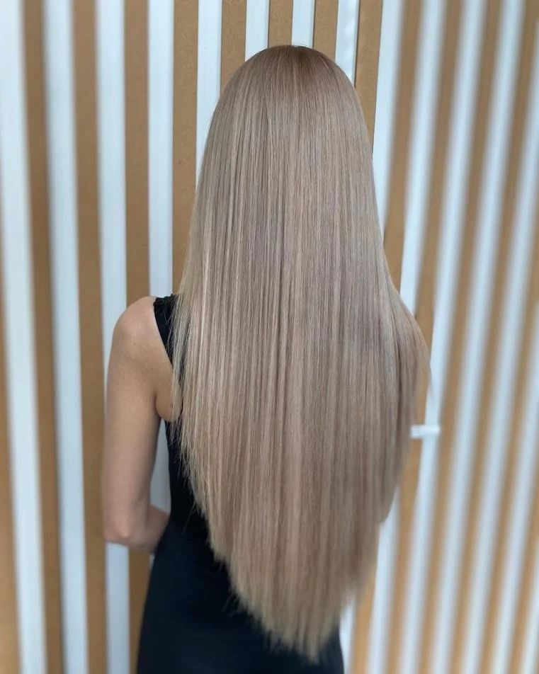 Długie, proste, popielate blond włosy, widok z tyłu, na tle ściany z pionowymi panelami w odcieniach beżu i bieli.