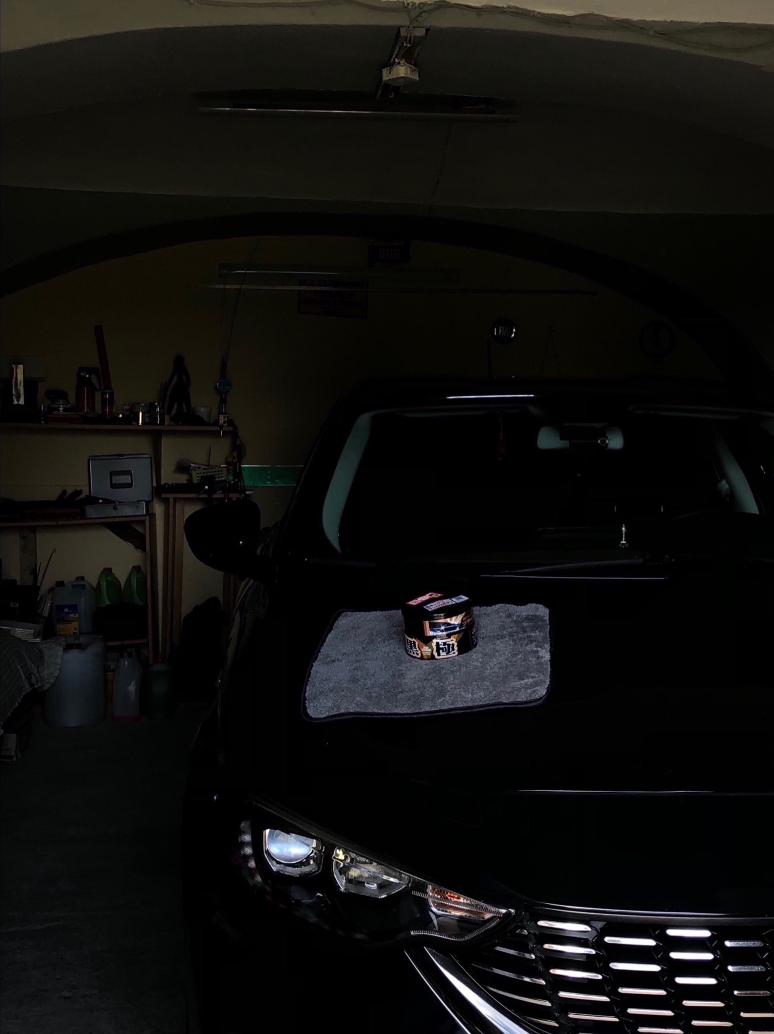 Ciemne ujęcie samochodu w garażu z produktem do detailingu na masce, leżącym na szarej ściereczce z mikrofibry.