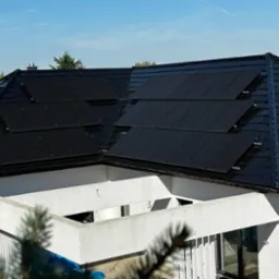 Czarny dach z panelami słonecznymi na nowoczesnym białym domu w słoneczny dzień.