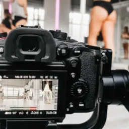 Kamera na gimbalu rejestruje nagranie wideo z zajęć pole dance; widoczny podgląd na ekranie z ustawieniami ekspozycji.