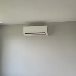 Biały klimatyzator LG Smart Inverter zamontowany na szarej ścianie w pomieszczeniu w Mąkoszycach, widok z boku, z oknem po lewej stronie.