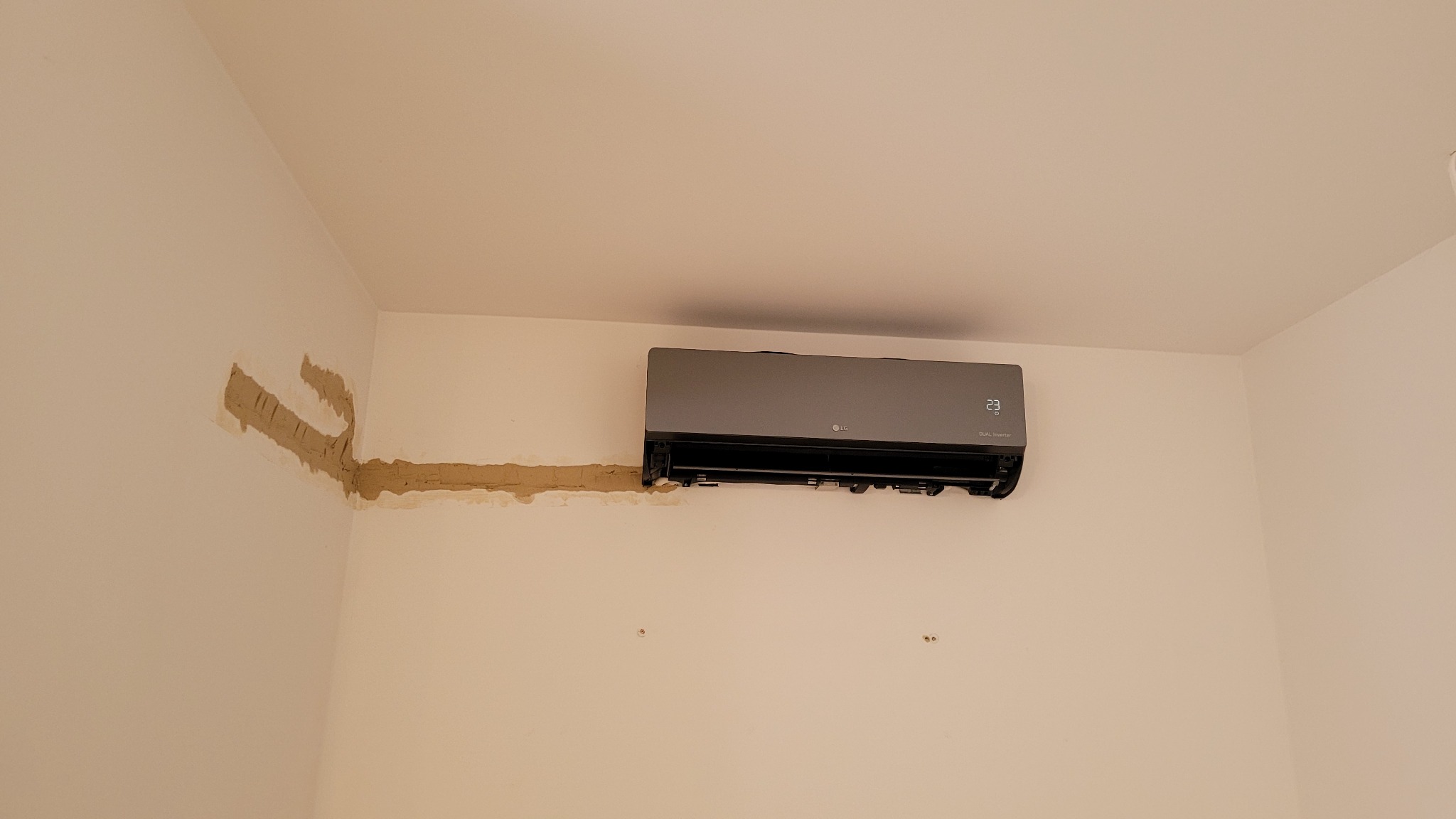 Szary klimatyzator LG typu split zamontowany na białej ścianie z widocznymi śladami po instalacji rur i przewodów, wypełnionymi gipsem.