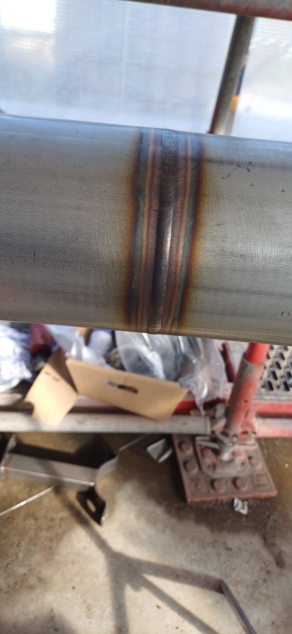 Spoina na rurze ze stali nierdzewnej, widoczne przebarwienia termiczne, fragment rusztowania w tle.