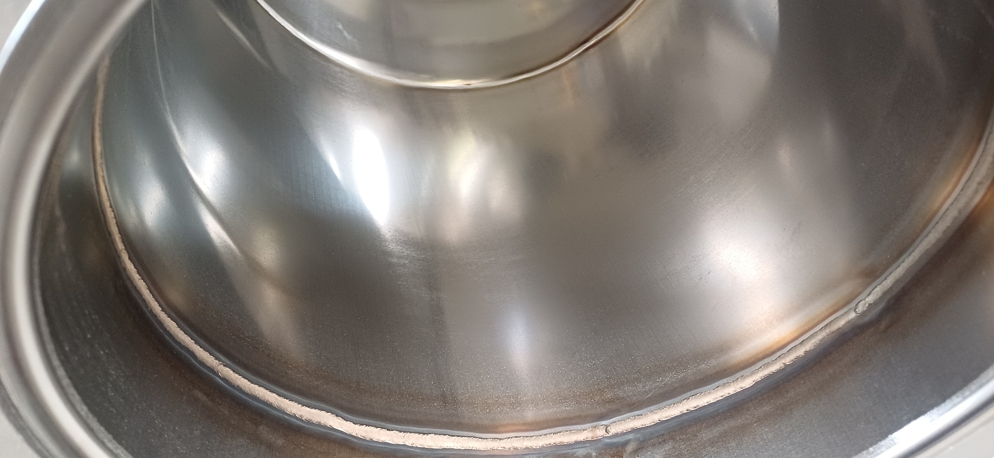 Wnętrze metalowego zbiornika ze śladami spoiny, widoczne refleksy światła na gładkiej powierzchni.