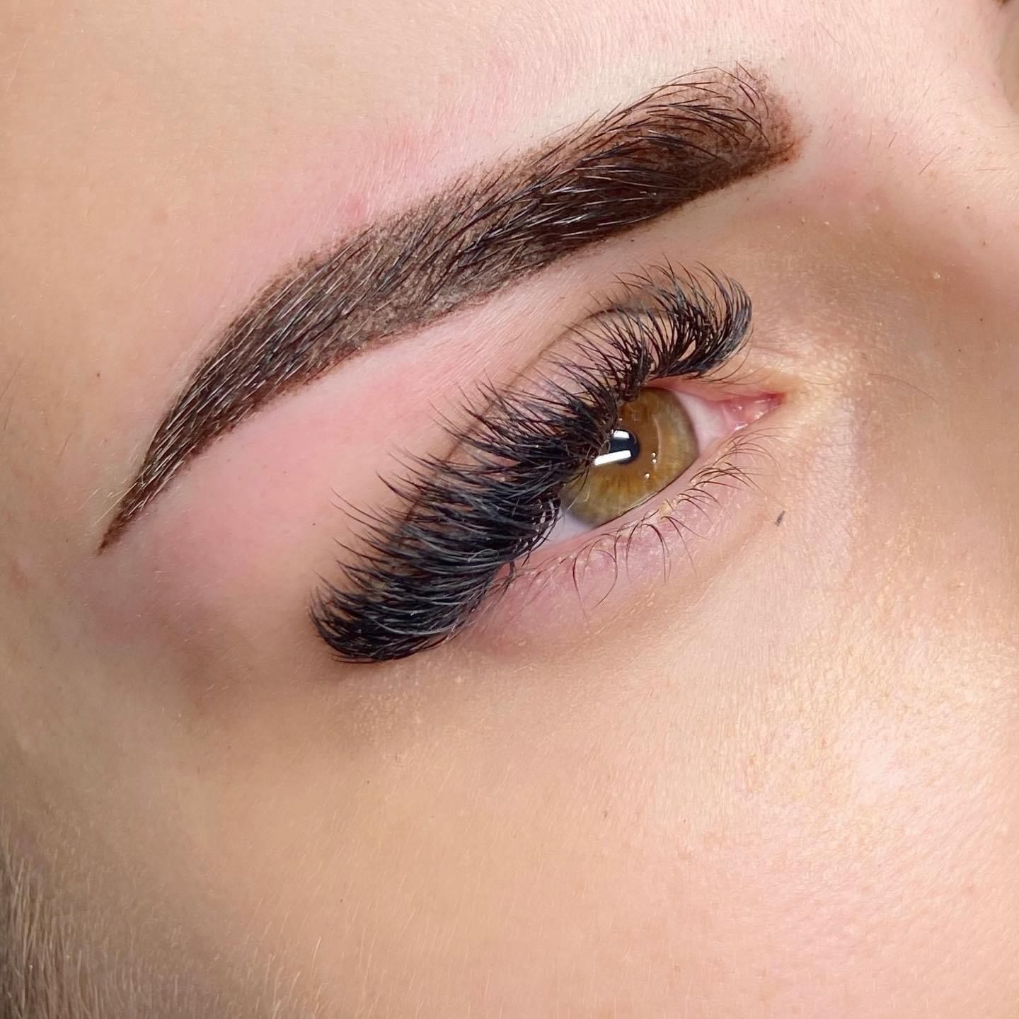 Zbliżenie na oko z gęstymi, przedłużonymi czarnymi rzęsami i wyregulowanymi brwiami z efektem pudrowego cienia.