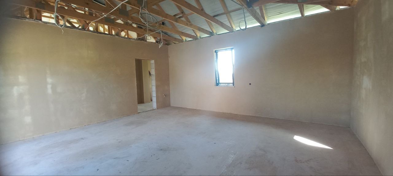 Wnętrze w trakcie prac wykończeniowych w Krakowie, ściany po nałożeniu wstępnej warstwy gładzi, widoczna surowa konstrukcja dachu i okno.