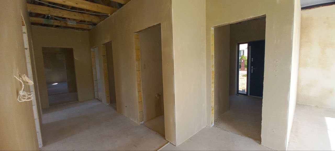 Surowe tynki maszynowe na ścianach w nowym domu, widoczne instalacje elektryczne i drewniana konstrukcja stropu, stan surowy zamknięty.