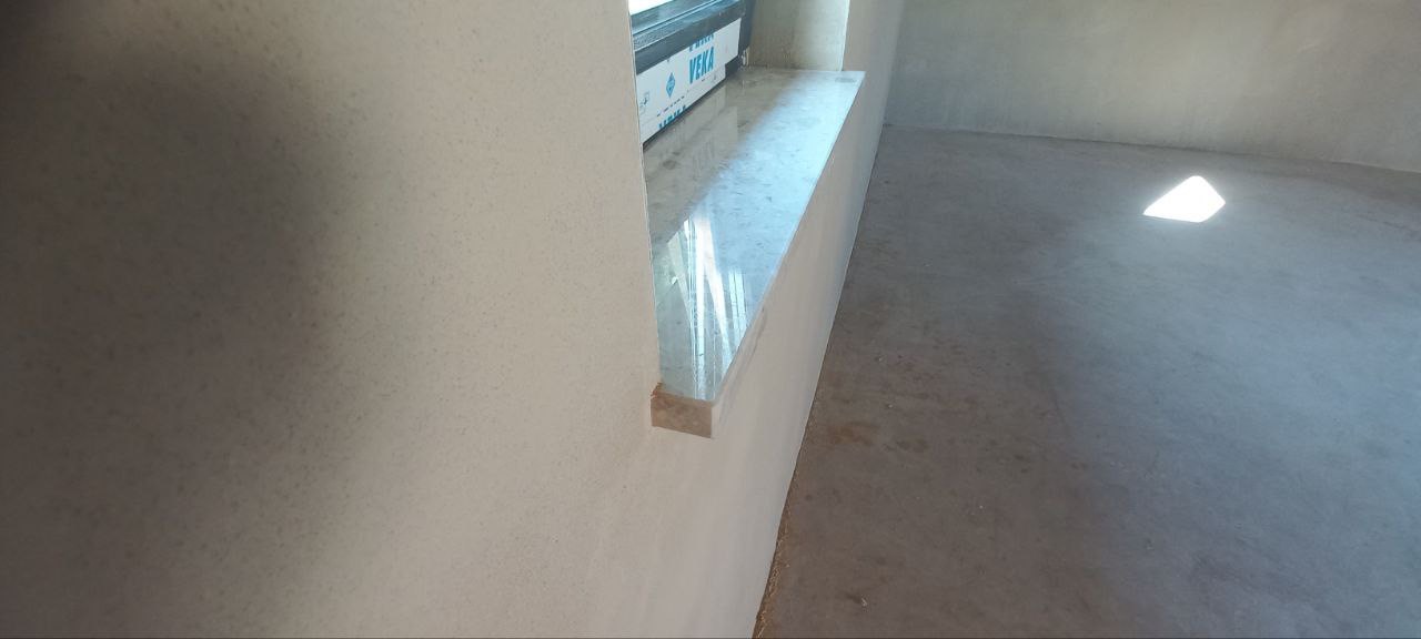 Świeżo nałożony, jasnoszary tynk maszynowy na ścianie wewnętrznej z widocznym parapetem okiennym z połyskiem i surową posadzką w pomieszczeniu w trakcie remontu.