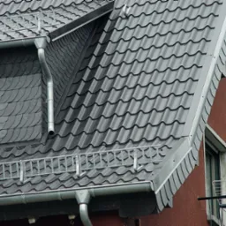Szary dach dwuspadowy z metalową dachówką i orynnowaniem, fragment ściany z oknem, w którym widać kaczkę.