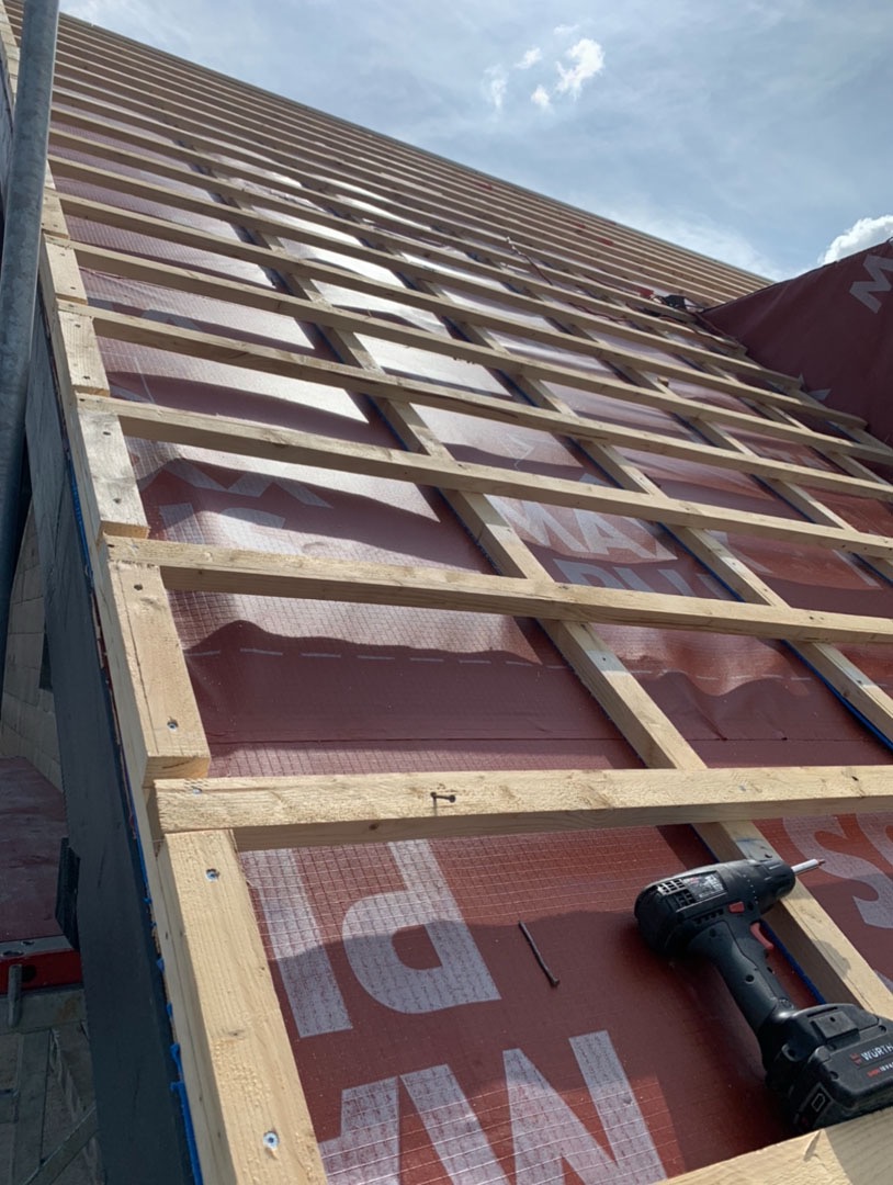 Konstrukcja więźby dachowej z widoczną membraną dachową, częściowo zamontowana, z wkrętarką akumulatorową i gwoździem leżącymi na membranie.