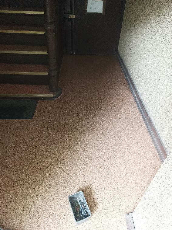 Korytarz po remoncie z nową, brązową podłogą z drobnego granulatu, widoczne schody z ciemnego drewna i puszka po farbie na podłodze.