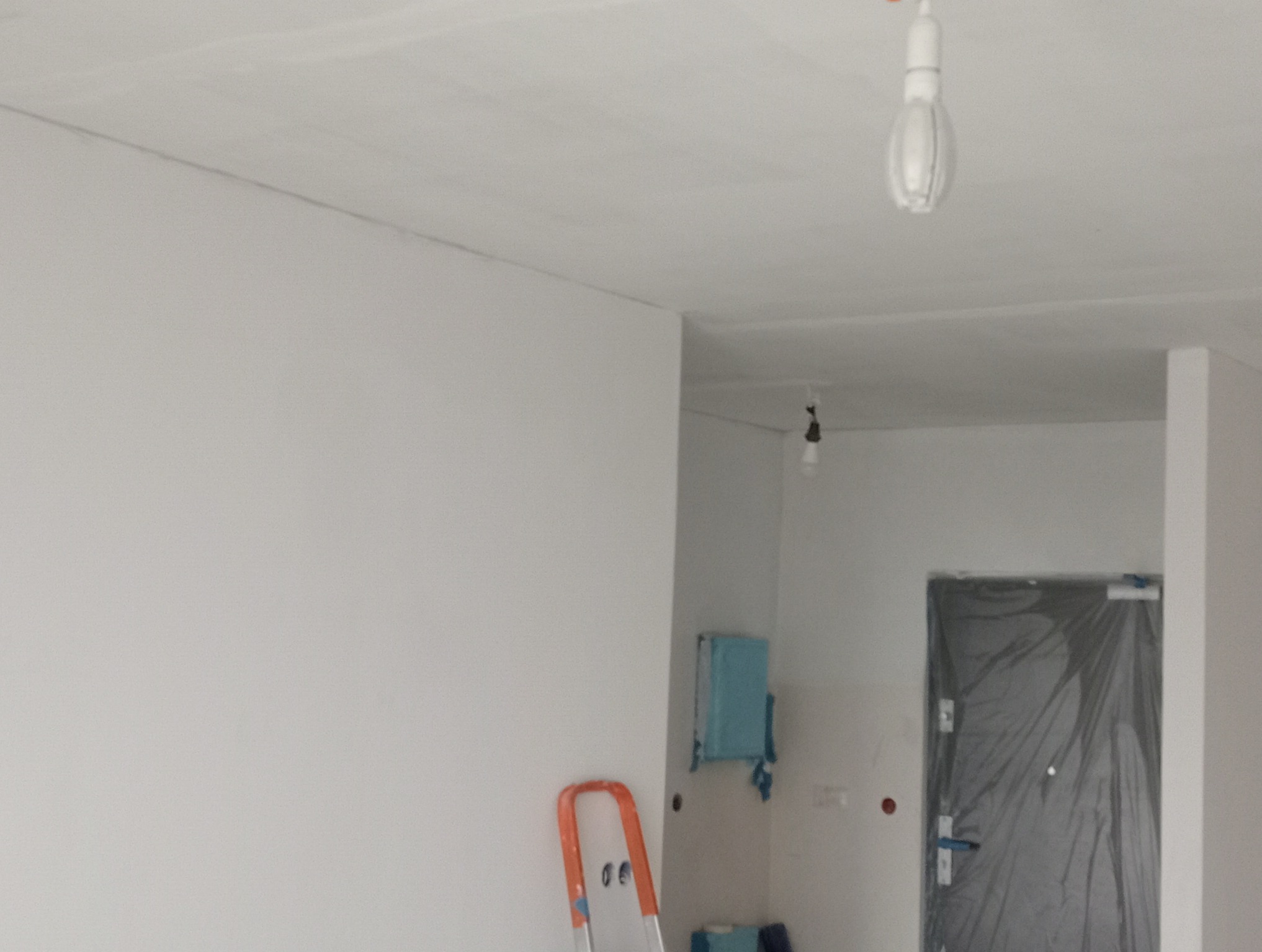 Świeżo pomalowane białe ściany i sufit w trakcie prac wykończeniowych, drabina oparta o ścianę, zabezpieczone folią drzwi w tle.