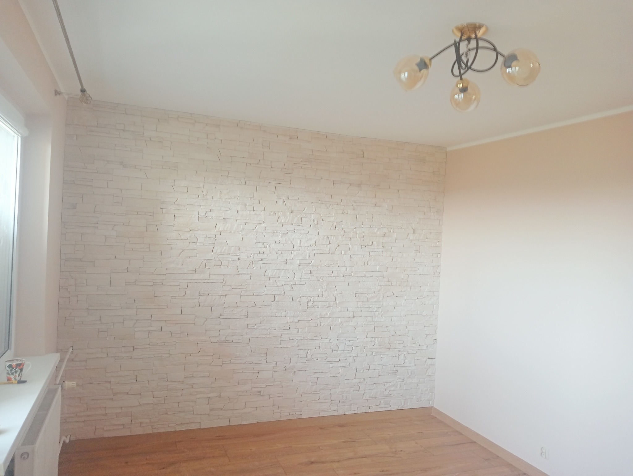 Wykończone wnętrze pokoju z dekoracyjną ścianą z białej cegły, drewnianą podłogą i nowoczesną lampą sufitową z żarówkami w stylu Edison