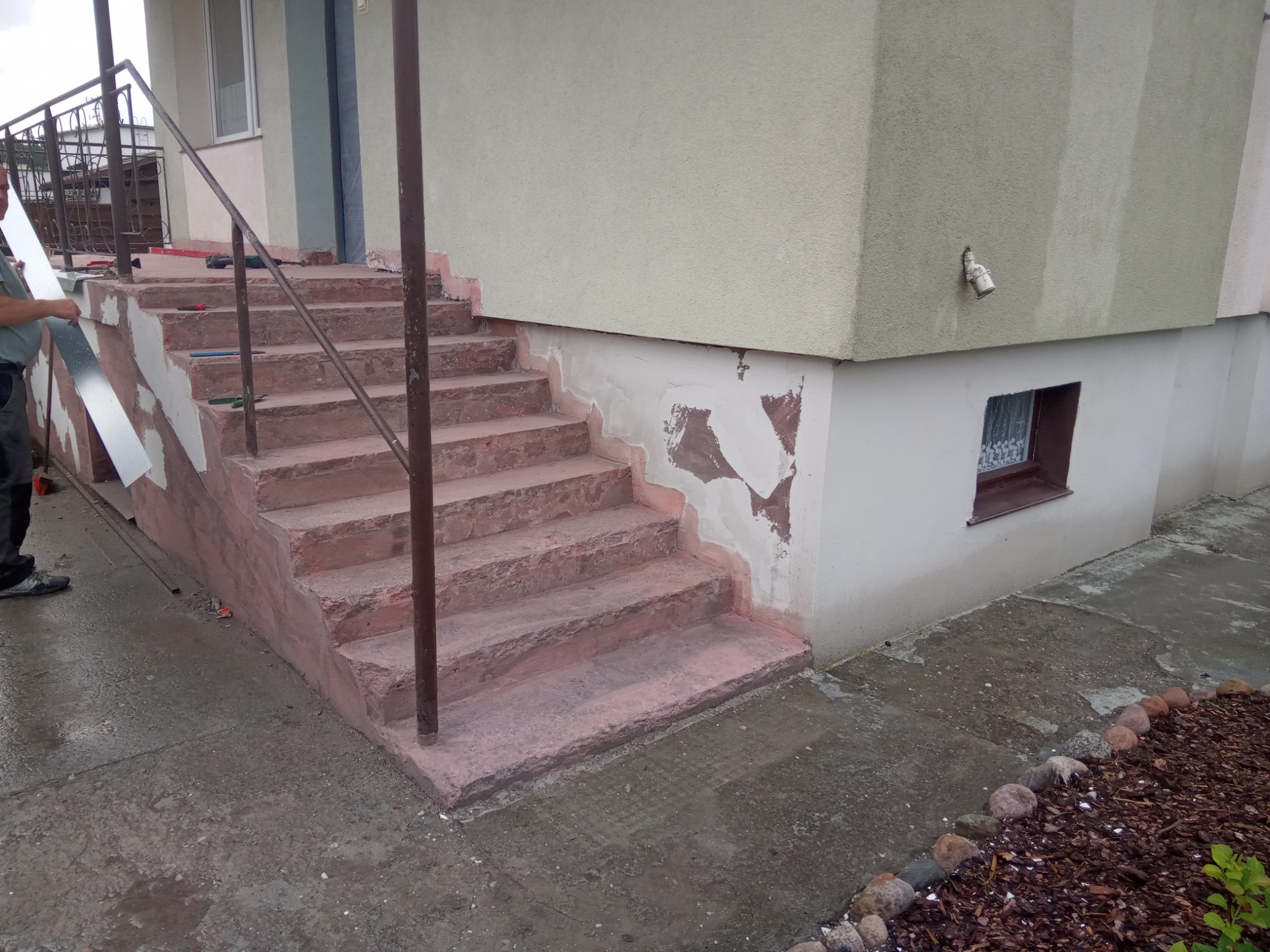 Remont schodów wejściowych: przygotowanie do położenia gładzi na uszkodzonych fragmentach, widoczne narzędzia i pracownik.