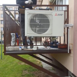 Kamil Matylek Klimat montaż serwis sprzedaż klimatyzacji i wentylacji - Montaż zewnętrznej jednostki klimatyzacji Mitsubishi Electric na balkonie, widoczne narzędzia i osprzęt instalacyjny, w tle budynek mieszkalny.