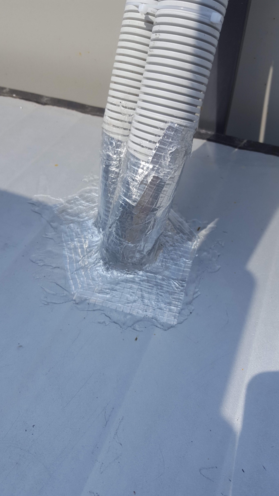 Dwa białe przewody klimatyzacji zabezpieczone srebrną taśmą na szarym dachu w Kraszowie.